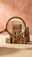 Magnifying glass focusing on wooden blocks with business growth icons and text against warm coral background for corporate development concepts.