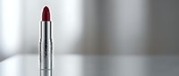 Deep burgundy lipstick in silver tube on white surface with soft lighting and blurred background for beauty and cosmetics marketing campaigns.