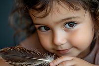 Young girl with brown eyes holding feather close to face, gentle smile, soft natural lighting, childhood innocence and wonder concept for parenting content.