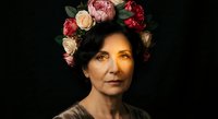 Middle-aged woman with floral crown of roses and peonies against dark background, elegant portrait with dramatic lighting for artistic projects.