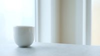 White ceramic cup on marble surface with soft natural light and blurred background, suitable for home decor, kitchenware, and lifestyle design projects.