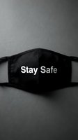 Black fabric face mask with Stay Safe text lying on dark gray surface, monochrome flat lay conveying health awareness and protection.