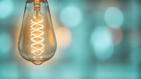 Vintage Edison bulb with spiral filament glowing warmly against soft turquoise bokeh background for modern interior design and lighting concepts.