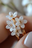 Delicate white mother of pearl flowers with golden stamens on elegant ring, macro photography showing fine jewelry craftsmanship against soft blurred background.