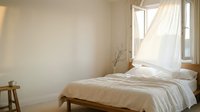 Minimalist bedroom with natural light streaming through window, featuring wooden bed frame, white bedding, and sparse decor for serene interior design projects.