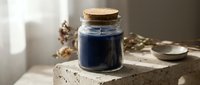Glass jar with cork lid containing dark blue liquid on concrete surface with natural lighting and dried botanicals for apothecary crafting projects.