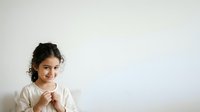 Young girl with dark curly hair and olive complexion wearing casual white shirt, smiling at camera against neutral background. Suitable for educational, family, and lifestyle marketing materials.