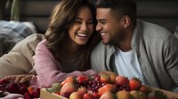 Young Hispanic couple sharing intimate moment on couch with fresh fruits. Genuine emotions, natural lighting creates warm atmosphere for lifestyle and relationship content.