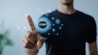 Young Asian male in black t-shirt pointing at glowing digital start button with floating technology icons, representing digital transformation and future interface concept.