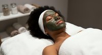 Young African American woman relaxing with green clay facial mask during spa treatment. Professional skincare and wellness therapy session.