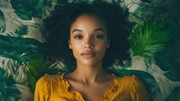 Young African American woman with natural curly hair wearing yellow dress against tropical leaves background, soft natural lighting creates dreamy atmosphere.