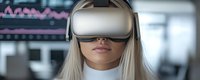 Young woman with long blonde hair wearing virtual reality headset against blurred office background with financial charts and graphs on display.