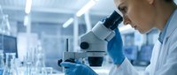 Female scientist in blue gloves examining samples through microscope in modern laboratory for medical research and scientific discovery.