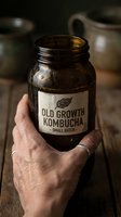 Hand holding a small batch fermented kombucha jar with vintage label, rustic wooden background, artisan probiotic drink concept.