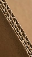 Corrugated cardboard edge showing detailed fluted structure and layers in warm brown tones for packaging and shipping industry applications.
