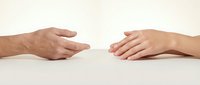 Two hands reaching toward each other across white surface showing connection, support, help, assistance, teamwork, cooperation, unity, trust, partnership.