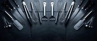 Professional kitchen utensils and tools arranged in semicircle on dark slate background for culinary cooking and food preparation concepts.