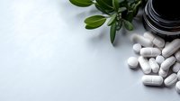 White pharmaceutical pills and capsules with green plant and dark container on clean white background for healthcare and medicine concept.
