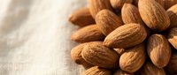 Pile of raw almonds on light linen fabric, suitable for food photography, nutrition content, healthy snacking, recipe blogs, and culinary publications.
