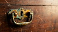 Antique brass keyhole with ornate handle on weathered wooden surface. Vintage lock mechanism shows patina and age for restoration projects.