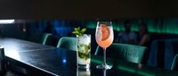 Two elegant cocktails on dark bar counter in upscale lounge with mojito and grapefruit drink featuring fresh garnishes for hospitality and nightlife concepts.