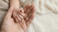 Adult hands gently holding tiny newborn baby hand in protective gesture. Tender moment between parent and infant showing care, love and family bond.