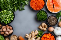 Fresh healthy ingredients arranged in bowls including salmon, red lentils, herbs, ginger root, eggs and vegetables on gray background with copy space for menu design.