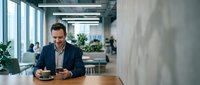 Professional businessman using smartphone in modern office workspace with natural lighting and contemporary design for business communication.