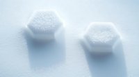 Hexagonal white sugar crystals casting soft shadows on light blue surface, minimalist food photography composition for culinary and sweetener concepts.