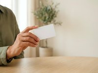 Adult male with medium skin tone holding blank white business card at wooden table, suitable for corporate branding, business identity, and professional marketing materials.