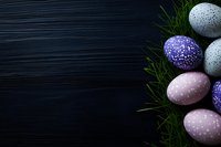 Decorated Easter eggs in gray, purple, and pink with polka dot patterns arranged on fresh green grass against dark wooden background with copy space.