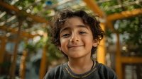 Young mixed-race boy with curly hair smiling warmly at camera in bright indoor playground setting with colorful equipment and natural lighting.