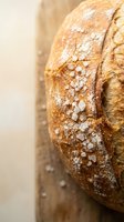 Artisan sourdough bread loaf with coarse sea salt crystals on golden crust, freshly baked on wooden cutting board for bakery and culinary content.