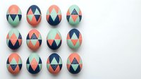 Colorful geometric Easter eggs with modern triangular patterns in coral, navy, and mint green arranged in rows on white background for spring holiday decor.