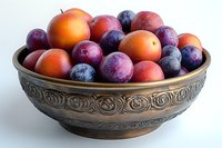 Fresh plums and apricots in antique bronze bowl with ornate floral pattern design against white background, natural organic summer fruits for healthy eating.