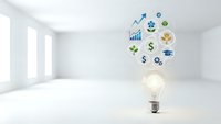 Light bulb with business icons floating above in modern white room representing innovation and financial growth concepts for presentations.