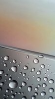 Water drops on metallic gray surface against soft pastel background, creating minimalist composition with natural light reflection and shadow patterns.