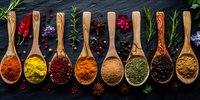 Colorful aromatic spices and herbs in wooden spoons arranged in row on black slate background, fresh ingredients for cooking and seasoning food preparation.
