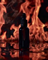 Dark glass dropper bottle against dramatic fire background with water reflection creates mysterious atmosphere for luxury product photography and advertising.