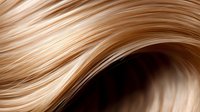 Flowing golden blonde hair strands in smooth waves creating elegant curves and highlights against dark background, macro close-up view for beauty and haircare concepts.