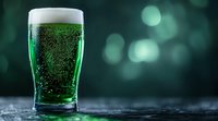 Green beer with bubbles and foam in pint glass on dark background with bokeh lights. St Patrick's Day celebration concept for bar menu and festive designs.