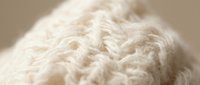 Close-up of natural cream-colored knitted fabric texture with detailed cable knit pattern, suitable for textile, fashion, and craft design projects.
