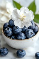 Fresh ripe blueberries in white ceramic bowl decorated with delicate jasmine flower, close-up on marble background. Food photography for healthy eating.