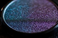 Shimmering holographic eyeshadow powder in compact with iridescent blue and purple tones for makeup and beauty applications.