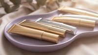 Luxury golden lipsticks arranged on elegant purple plate with soft lighting creating glamorous beauty cosmetics display for makeup and fashion concepts.