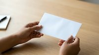Female hands holding blank white card on wooden desk with notebook and pen, suitable for business branding and stationery mockups.