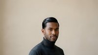 African American male professional in dark turtleneck against neutral beige background, suitable for corporate portraits, business profiles, and professional headshots.