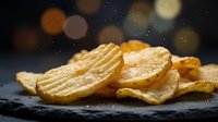 Golden crispy potato chips on dark slate surface with warm bokeh lights background creating festive snack food atmosphere for party celebrations.