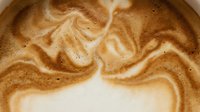 Latte art with swirled caramel and cream patterns in hot beverage, suitable for coffee shop menus, café marketing, and food photography projects.