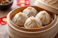 Steamed dumplings in traditional bamboo basket with pleated wrappers and juicy filling, served during Chinese New Year celebration with red envelopes in background.